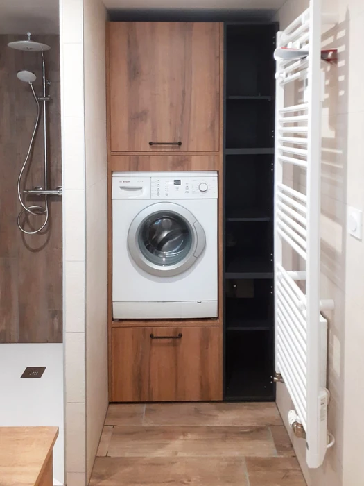Salle de bain avec colonne de rangement en bois imitation chêne intégrant un lave-linge Bosch frontal surélevé, encadré de portes avec poignées noires