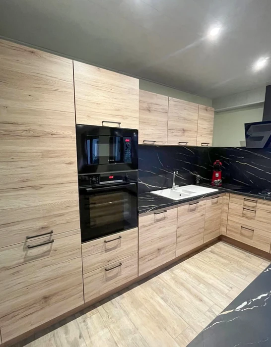 Cuisine moderne en L avec façades de meubles effet chêne naturel, plan de travail et crédence en marbre noir veiné blanc