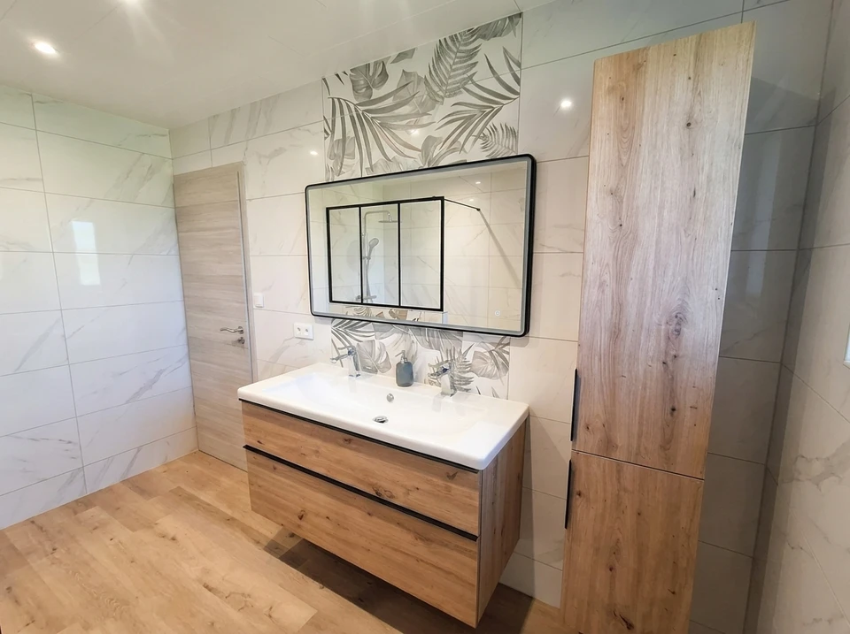 Un ouvrier en combinaison et casque de s&eacute;curit&eacute; blanc mesure une porte int&eacute;rieure blanche avec un m&egrave;tre ruban jaune dans un appartement moderne aux murs gris
