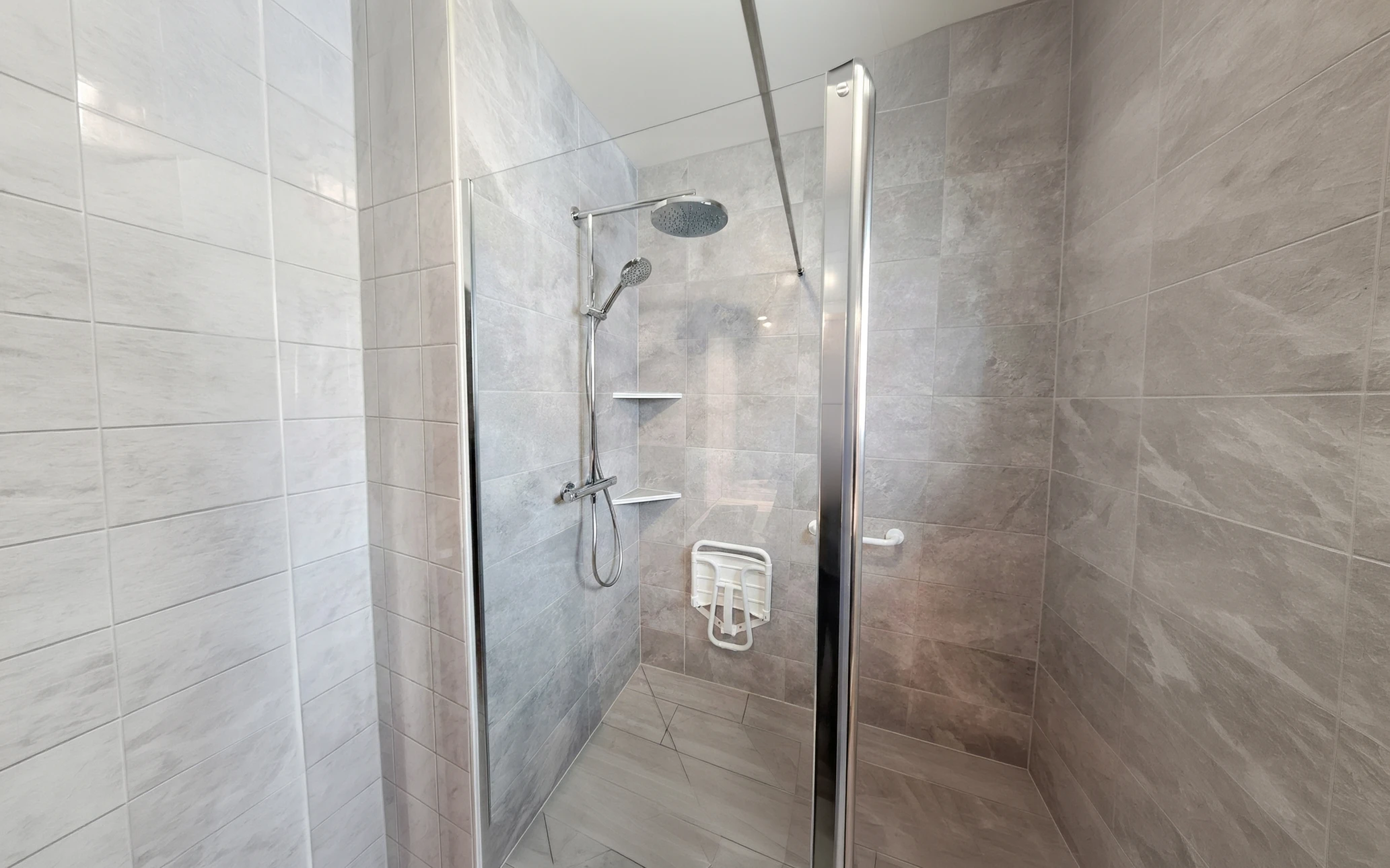 Salle de bain adaptée PMR avec toilettes suspendues blanches équipées de barres d'appui rabattables en acier inoxydable