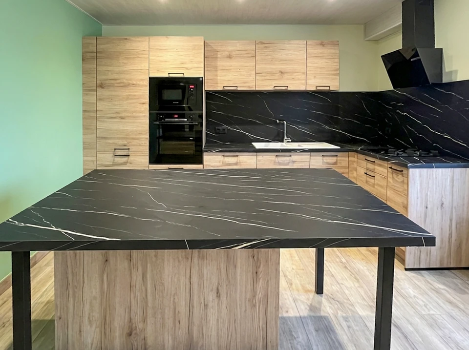 Photographie d'un chantier de rénovation intérieure montrant plusieurs artisans (plombier, électricien, carreleur, peintre) travaillant simultanément dans une cuisine ou salle de bain en cours de rénovation complète. Les ouvriers, vêtus professionnellement avec équipements de sécurité, collaborent harmonieusement sur différentes tâches (pose carrelage, installations sanitaires, peinture, travaux électriques) dans un espace en transformation, illustrant la maîtrise totale de l'exécution et la cohésion d'une équipe interne polyvalente.