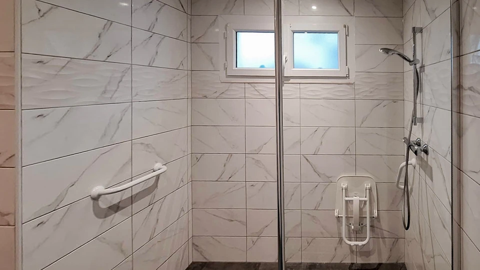 Équipe de plusieurs artisans professionnels travaillant ensemble sur un chantier de rénovation intérieure. On voit un menuisier installant un meuble sur mesure en bois, un plombier vérifiant des tuyauteries, et un peintre travaillant en arrière-plan dans une pièce en cours de rénovation. La scène montre une cuisine ou salle de bain en transformation, avec des outils professionnels visibles, une atmosphère de travail coordonné et concentré. Les artisans portent des vêtements de travail appropriés. La composition transmet la professionnalité, la cohésion d'équipe et le savoir-faire métier.