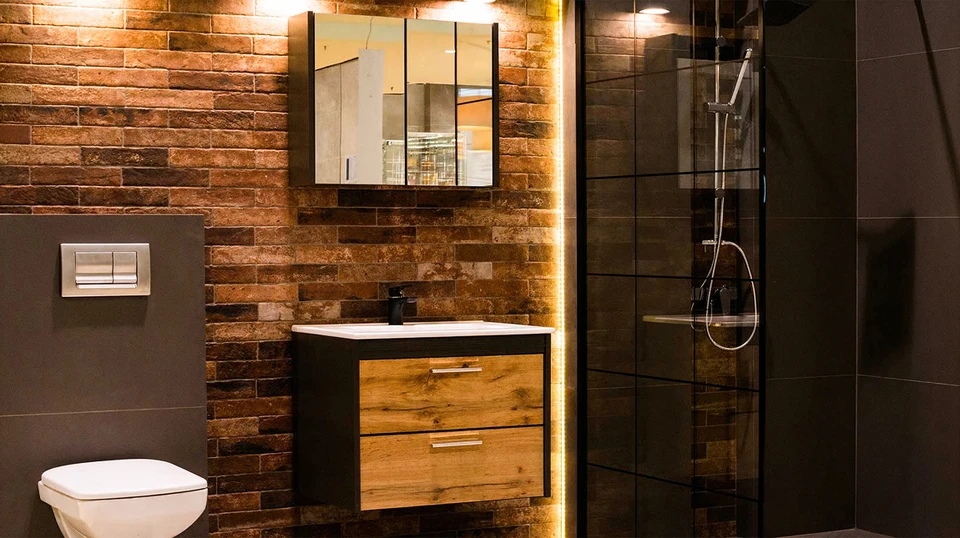 Gros plan d'un carreleur professionnel en tenue de travail, depuis la taille vers le bas, en train de poser soigneusement des carreaux au sol à l'intérieur d'une cuisine ou d'une salle de bain. L'artisan utilise une spatule crantée et des outils de pose professionnels. On distingue des carreaux modernes et des joints bien alignés en cours de réalisation. L'arrière-plan montre un intérieur rénové avec murs clairs. La scène transmet la rigueur, la précision et le professionnalisme de la pose.